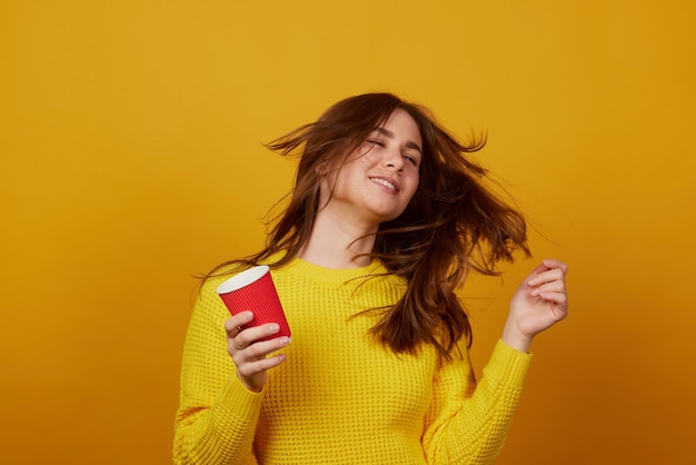 La niña sostiene un vaso desechable en la mano y se regocija con un fondo amarillo