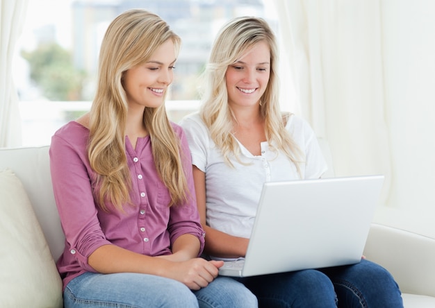 Una niña y su amiga mirando en una computadora portátil mientras está en el sofá