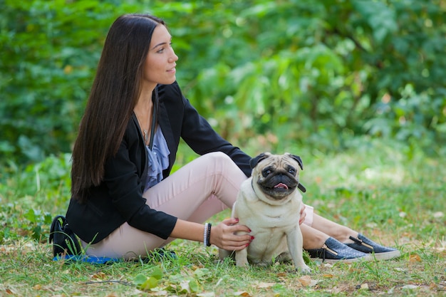 niña y su amigo de cuatro patas pug a dar un paseo. Los amigos están sentados en el suelo.