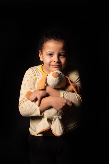 Niña con su animal de peluche, fondo negro, retrato de bajo perfil, enfoque selectivo.