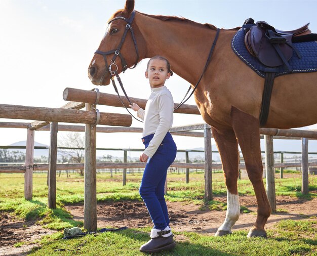 Una niña y su caballo Toma de cuerpo entero de una adorable niña de pie con su caballo afuera en el rancho