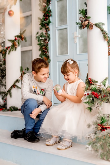 La niña y su hermano abren los regalos de Navidad. Los niños ven una bola de nieve sorpresa