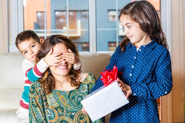 Niña con su hermano dando un regalo a su madre en el sofá de la sala de estar en casa