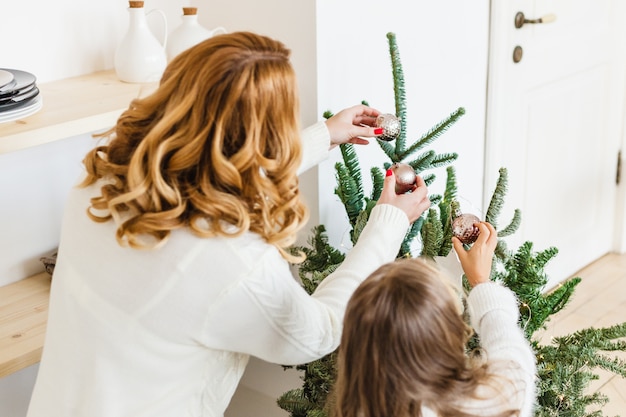 Una niña con su madre cerca del árbol de Navidad, interior decorado para Navidad