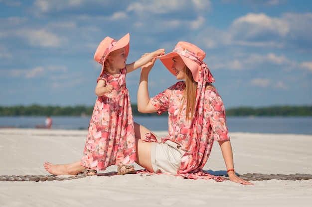 Una niña con su madre en hermosos vestidos de verano a juego juega en la arena de la playa. Aspecto familiar elegante.