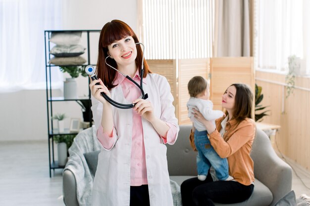 Niña con su madre en un médico en consulta. Feliz sonriente joven doctora en bata blanca uniforme y estetoscopio