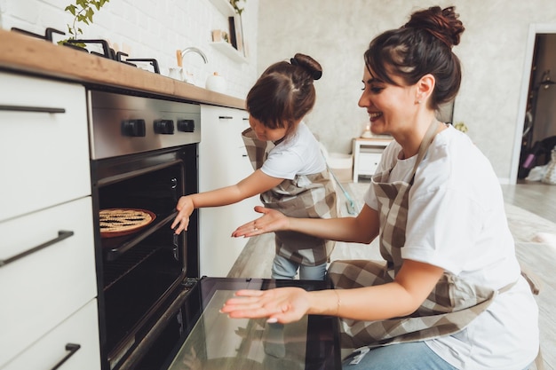 Foto una niña y su madre ponen una fuente para hornear con un pastel en el horno de la cocina, mamá y su hijo cocinan un pastel juntos en la cocina.