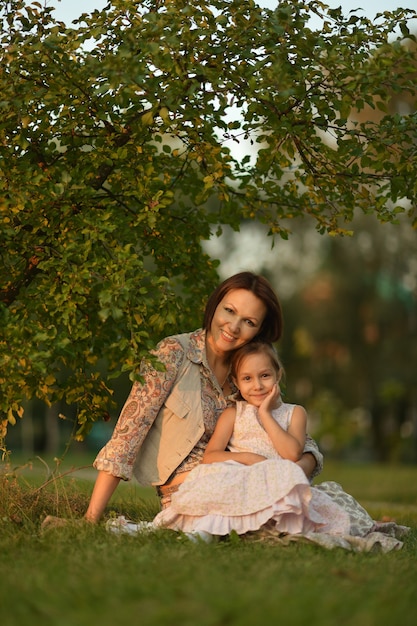 Niña con su madre sentada bajo un árbol en la naturaleza al atardecer