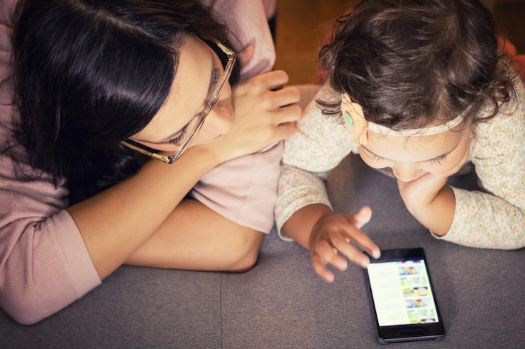 Foto niña con su madre usando el teléfono mientras se relaja en la cama en casa