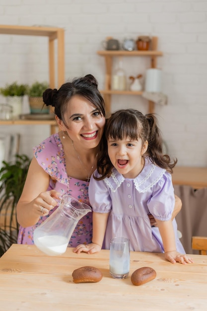 la niña y su madre vierten leche de una jarra en un vaso en la cocina