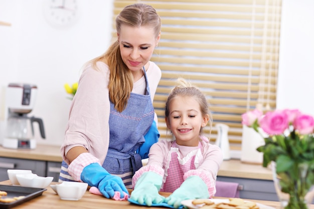 Niña y su mamá en delantales divirtiéndose limpiando la cocina