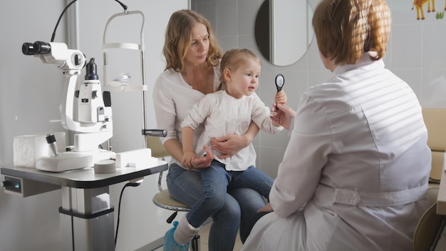 Niña y su mamá en oftalmología - optometrista comprobando la visión del niño pequeño, de cerca