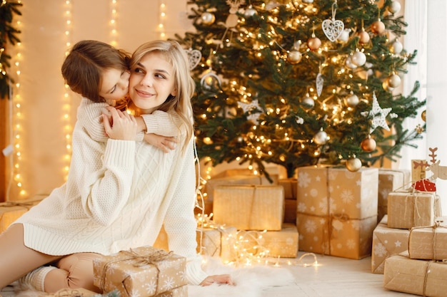 Niña y su mamá sentadas cerca del árbol de Navidad y abrazándose