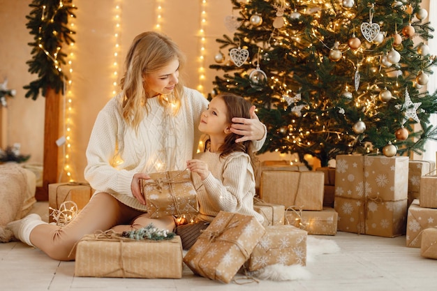 Niña y su mamá sentadas cerca del árbol de Navidad con caja de regalo