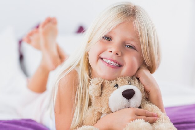 Niña con su oso de peluche acostado en una cama