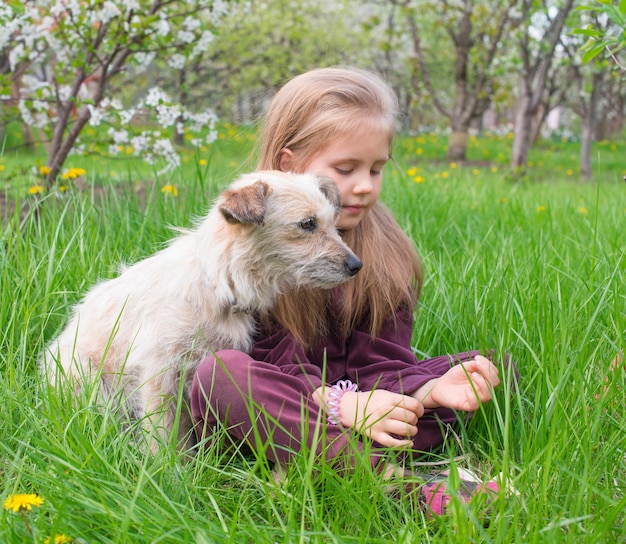 Niña con su perro mascota sentado al aire libre en la hierba