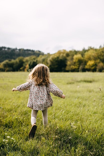 Niña suave y enfocada corriendo en un campo abierto con hierba verde con un vestido