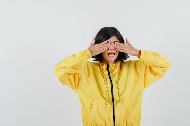 Niña en sudadera con capucha amarilla cogidos de la mano en los ojos y mirando emocionado, vista frontal.