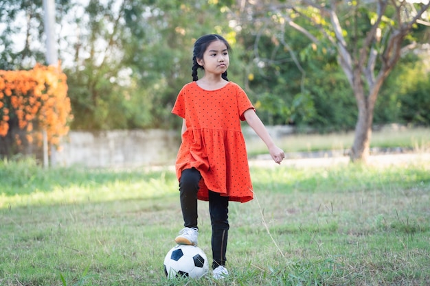 Una niña del sudeste asiático con el fútbol con su gran perro negro fuera del césped en el patio trasero por la noche. Concepto de amante de las mascotas