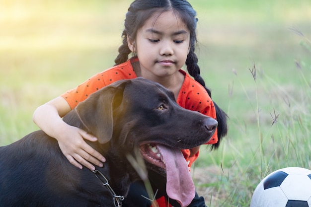 Una niña del sudeste asiático con el fútbol con su gran perro negro fuera del césped en el patio trasero por la noche. Concepto de amante de las mascotas