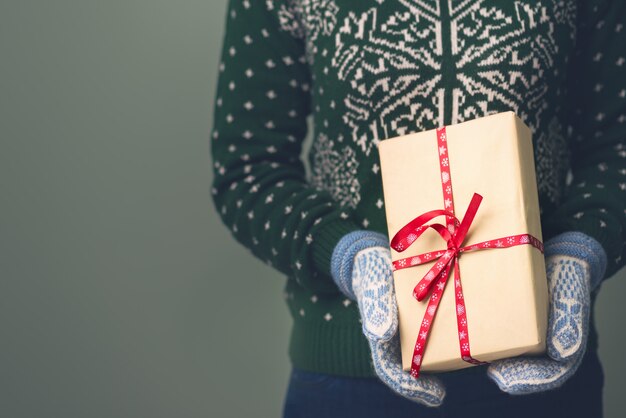 Una niña en un suéter de Año Nuevo tiene un regalo. Regalos para hombres. Feliz Navidad. Regalo para una niña. Suéter con adornos navideños. Vestido de punto.