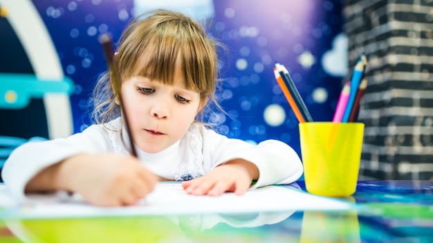 Una niña con un suéter blanco dibuja con entusiasmo con lápices