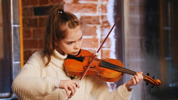 Una niña con suéter blanco tocando el violín.