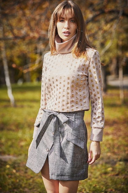 Una niña con un suéter y una falda de cuero en el fondo de un parque de otoño