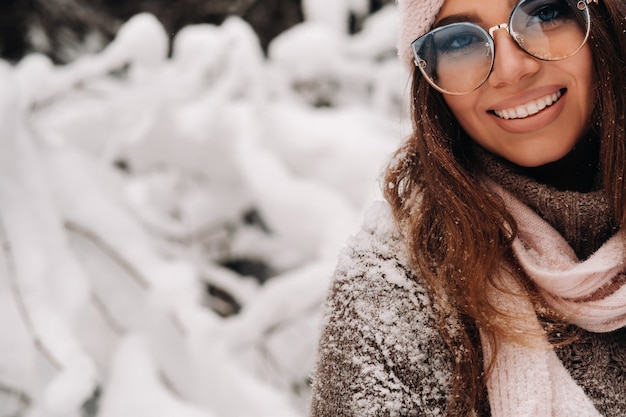 Una niña con un suéter y gafas en invierno en un bosque cubierto de nieve.