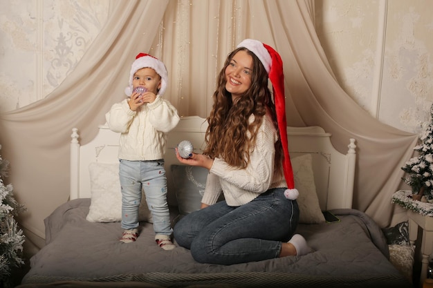 Una niña con un suéter con una hija pequeña con sombreros de Santa Claus sentada en la cama