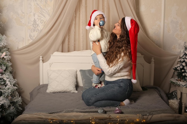 Una niña con un suéter con una hija pequeña con sombreros de Santa Claus sentada en la cama