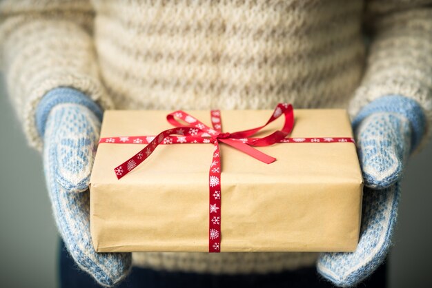 Una niña con un suéter de punto cálido y guantes está sosteniendo un regalo de Navidad.