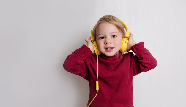 Foto una niña con un suéter rojo escucha música con auriculares y se ríe sobre un fondo blanco.