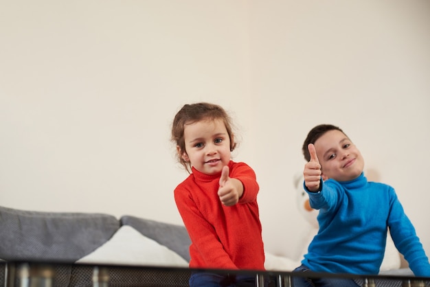 Foto una niña con suéter rojo sentada en el sofá cerca de un niño con suéter azul mostrando los pulgares hacia arriba y sonriendo a la cámara