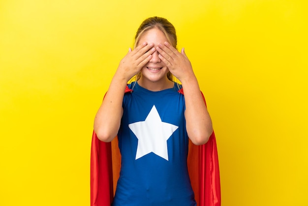 Niña superhéroe aislada sobre fondo amarillo que cubre los ojos con las manos