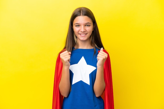 Niña superhéroe caucásica aislada de fondo amarillo celebrando una victoria en posición ganadora