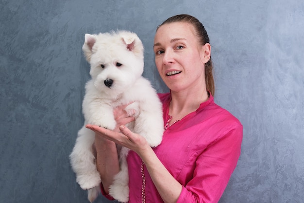 Una niña en sus brazos con un cachorro West Highland White Terrier sobre una pared gris