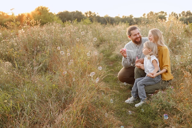 Una niña y sus padres con pompas de jabón en la naturaleza para divertirse.