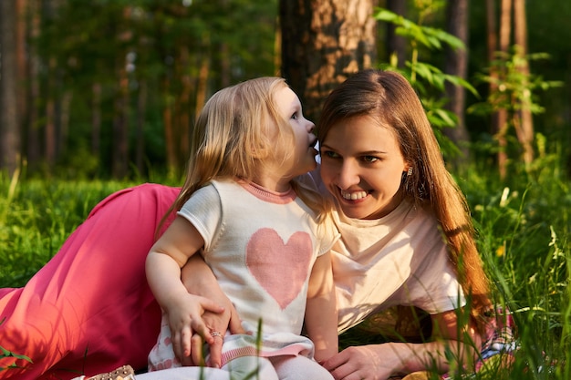 Niña susurra algo al oído de su madre durante un picnic en un bosque o parque