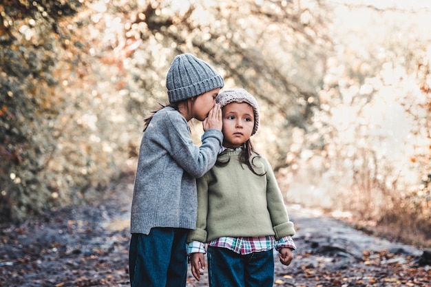 La niña le susurra un secreto a su hermana sentada en el contexto de la naturaleza. Amistad de hermanas