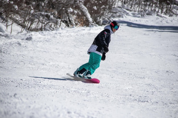 Una niña en una tabla de snowboard baja por la ladera de la montaña.