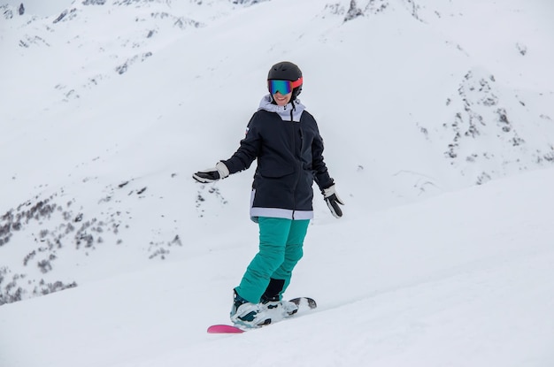 Una niña en una tabla de snowboard baja por la ladera de la montaña.