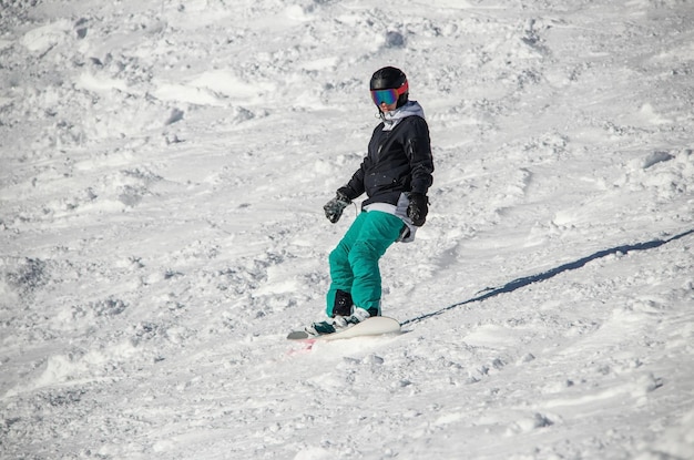 Una niña en una tabla de snowboard baja por la ladera de la montaña.