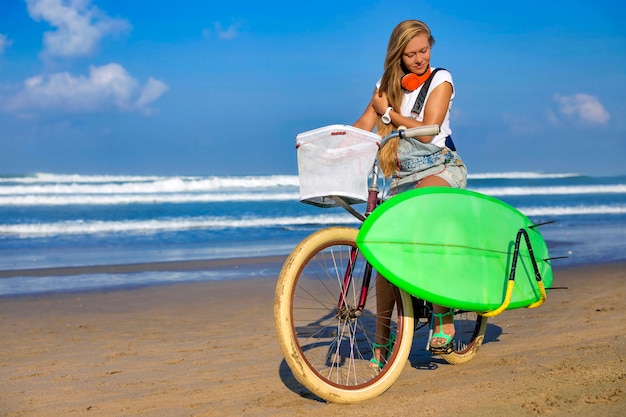 Niña con tabla de surf y bicicleta en la playa, Bali, Indonesia