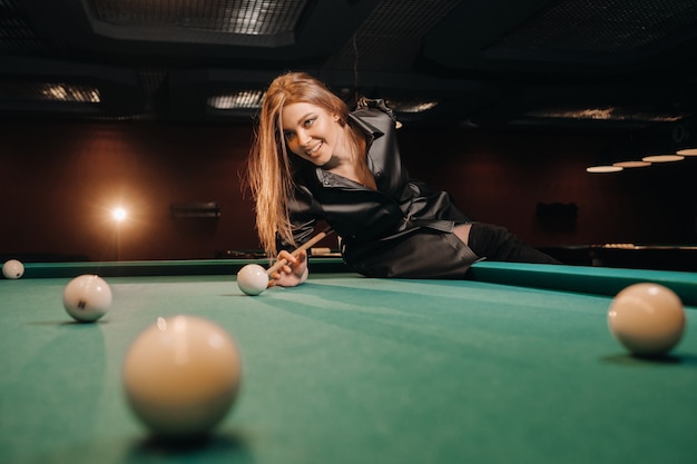 Una niña con un taco en sus manos hace un tiro a una bola en un club de billar. Billar ruso.