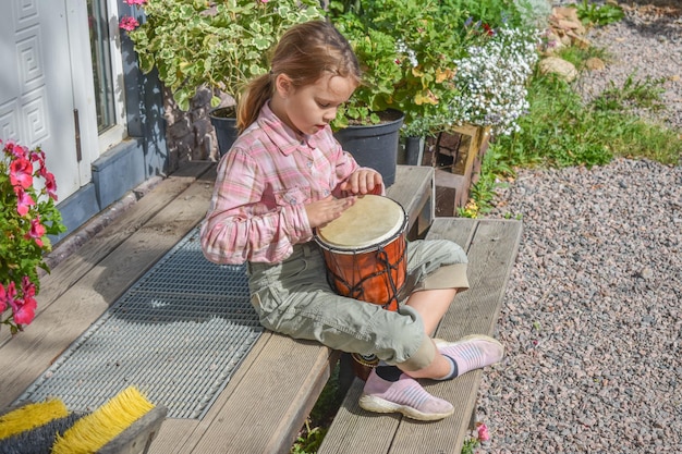 La niña con un tambor djembé al aire libre en el porche de la casa foto sin procesar