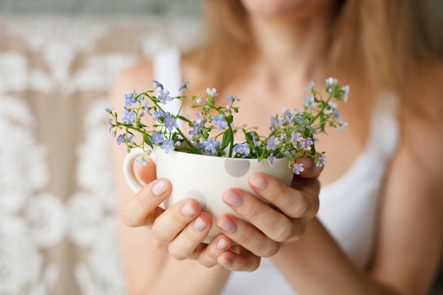 Niña en un tanque blanco sosteniendo una taza punteada con nomeolvides Flores en una taza Manos con flores