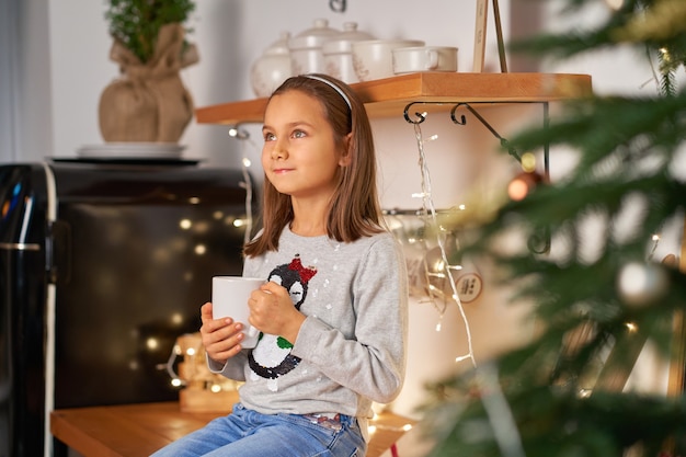 Una niña con una taza de té caliente sueña con un regalo de Papá Noel para Navidad