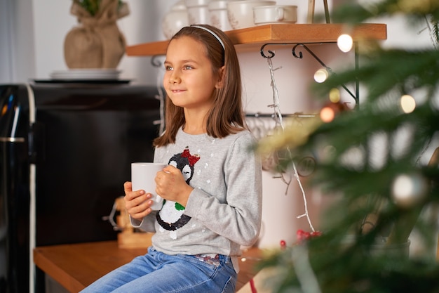 Una niña con una taza de té caliente sueña con un regalo de Papá Noel para Navidad