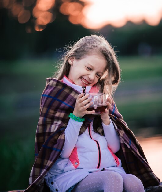 Niña con una taza de té en un picnic en un día fresco